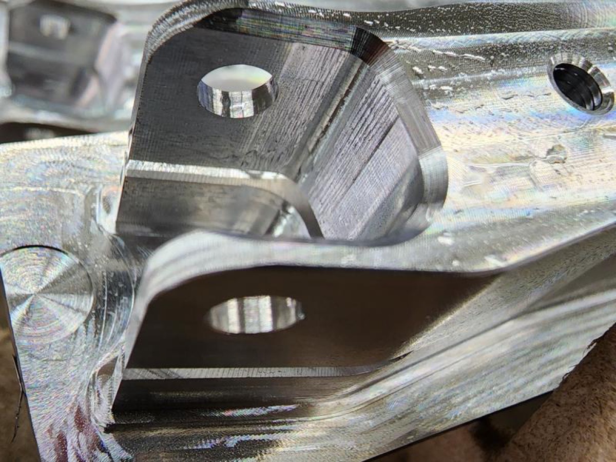 Machined aluminum bracket with a U-shaped slot and holes, sitting on a textured burlap-like material.